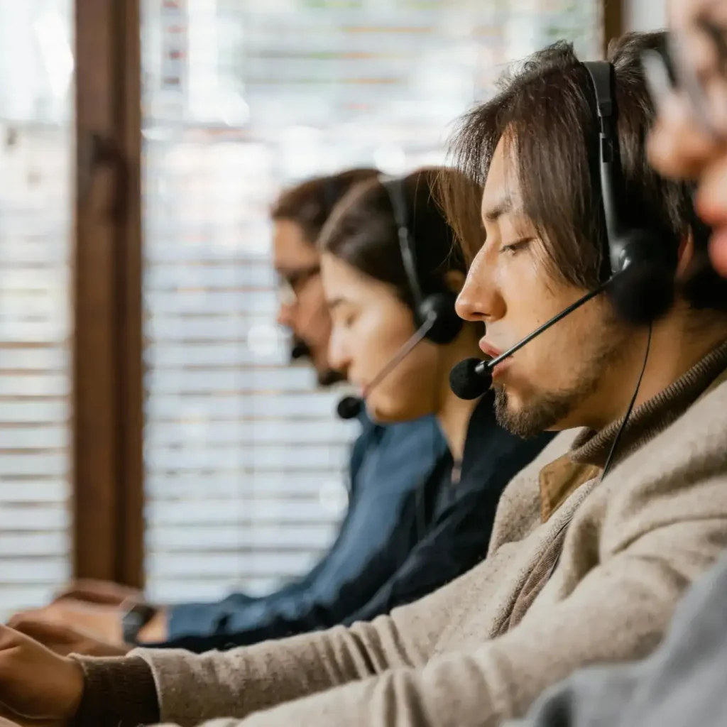 Team of people wearing headsets working on laptops in a call center environment.